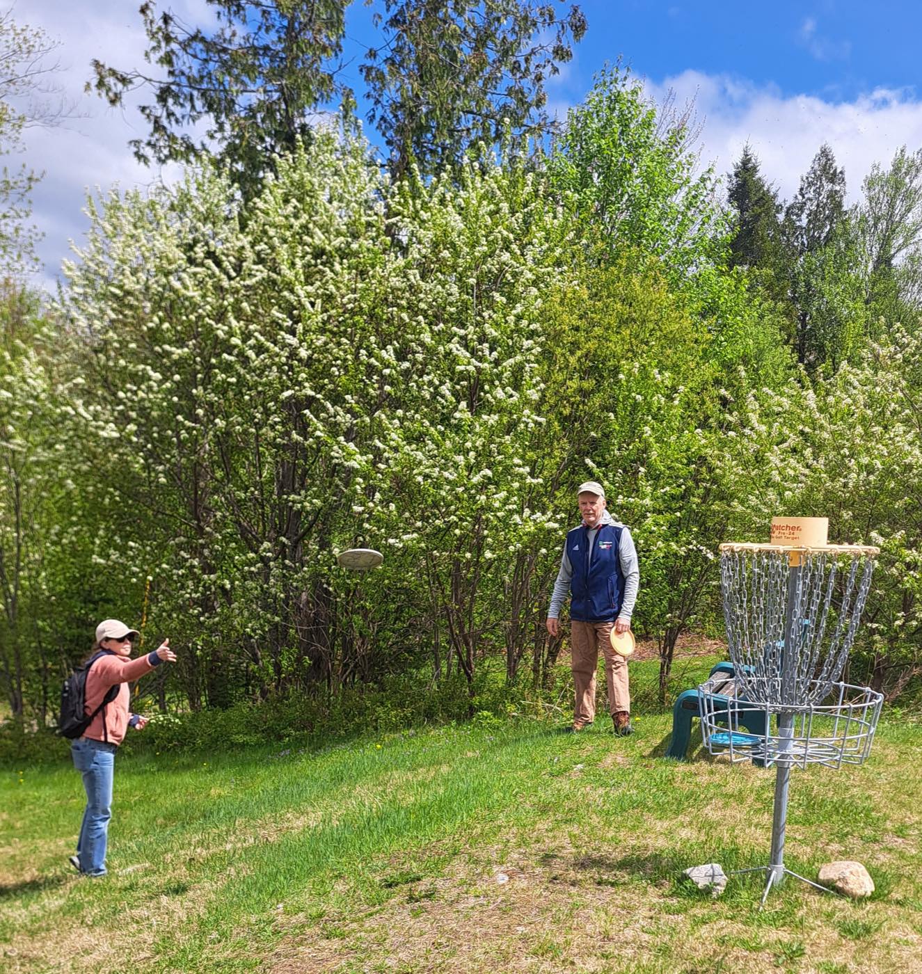 Two players on the FKOC disc golf course in spring, one mid-throw